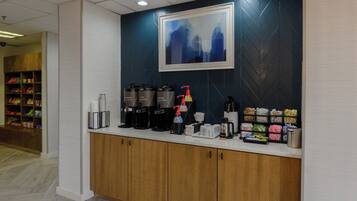 Zona de recepción con estación de café, dispensador de agua y un cuadro abstracto enmarcado en la pared.