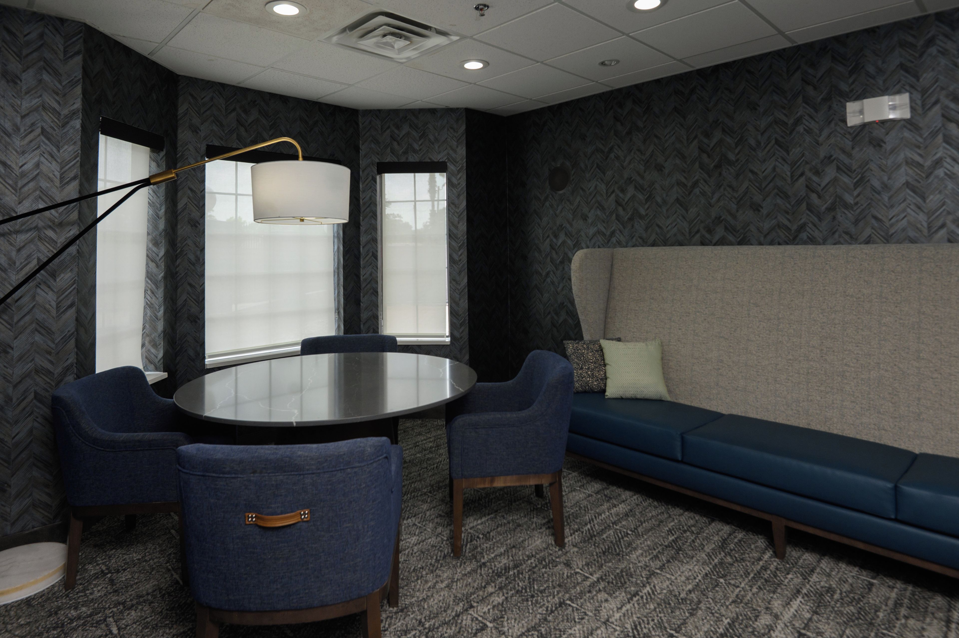 A conference room with a round table, two chairs, a sofa, and a lamp.