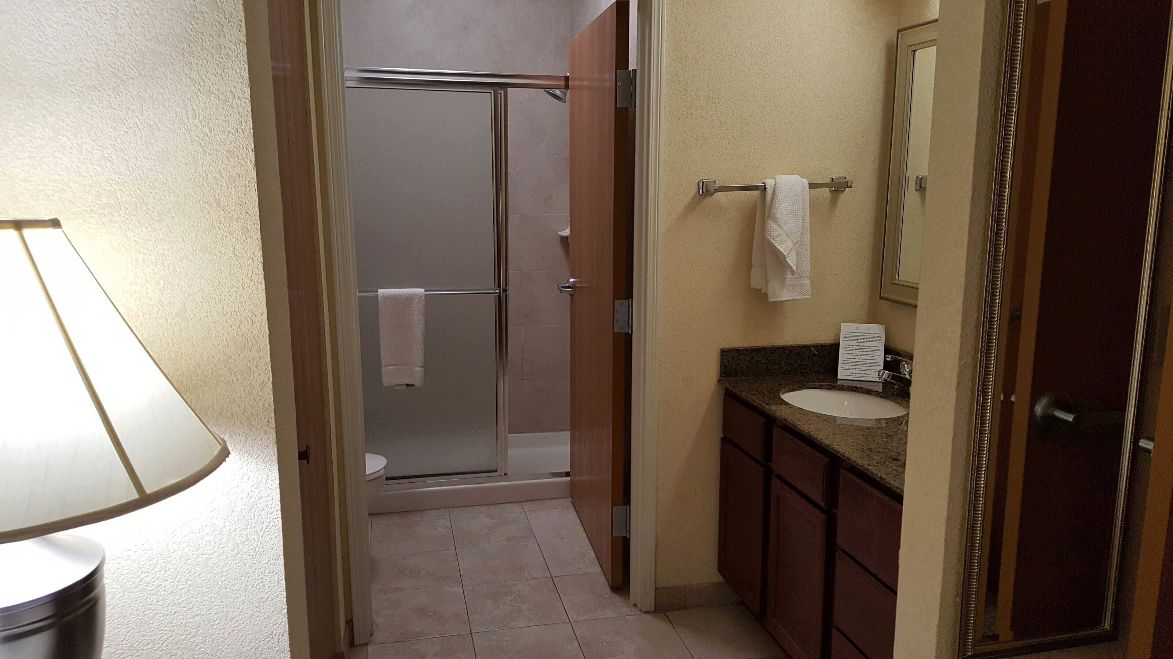 A narrow hallway leading to a bathroom with a shower, a sink, and a mirror.