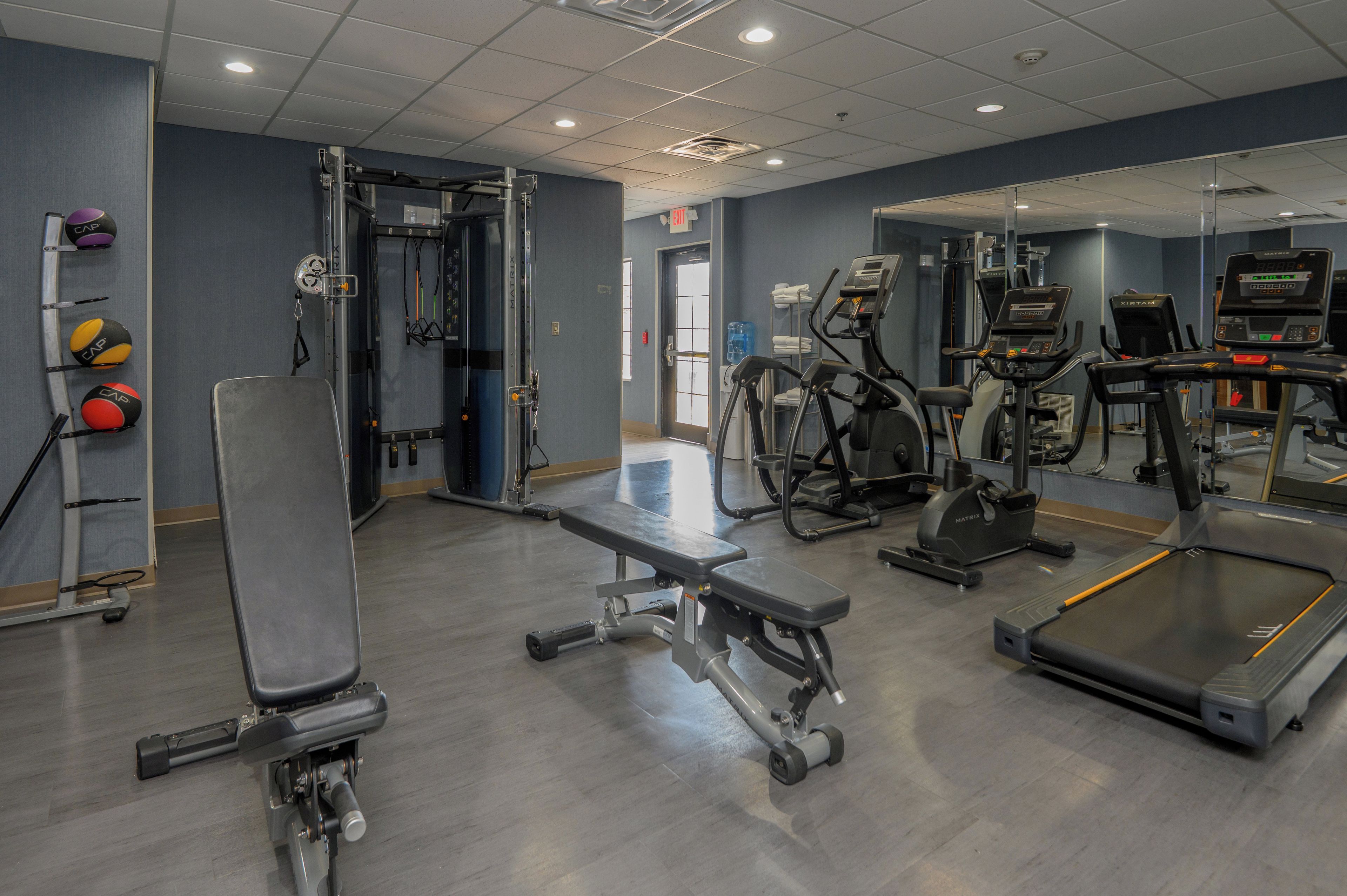 Un gimnasio con diverso equipamiento de ejercicio, incluyendo cintas de correr, máquinas de pesas y una banca.
