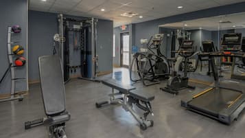 A gym with various exercise equipment, including treadmills, weight machines, and a bench.