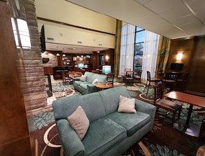 A hotel lobby with a sofa, dining area, and kitchen in the background. - Staybridge Suites Corpus Christi by IHG (Corpus Christi)