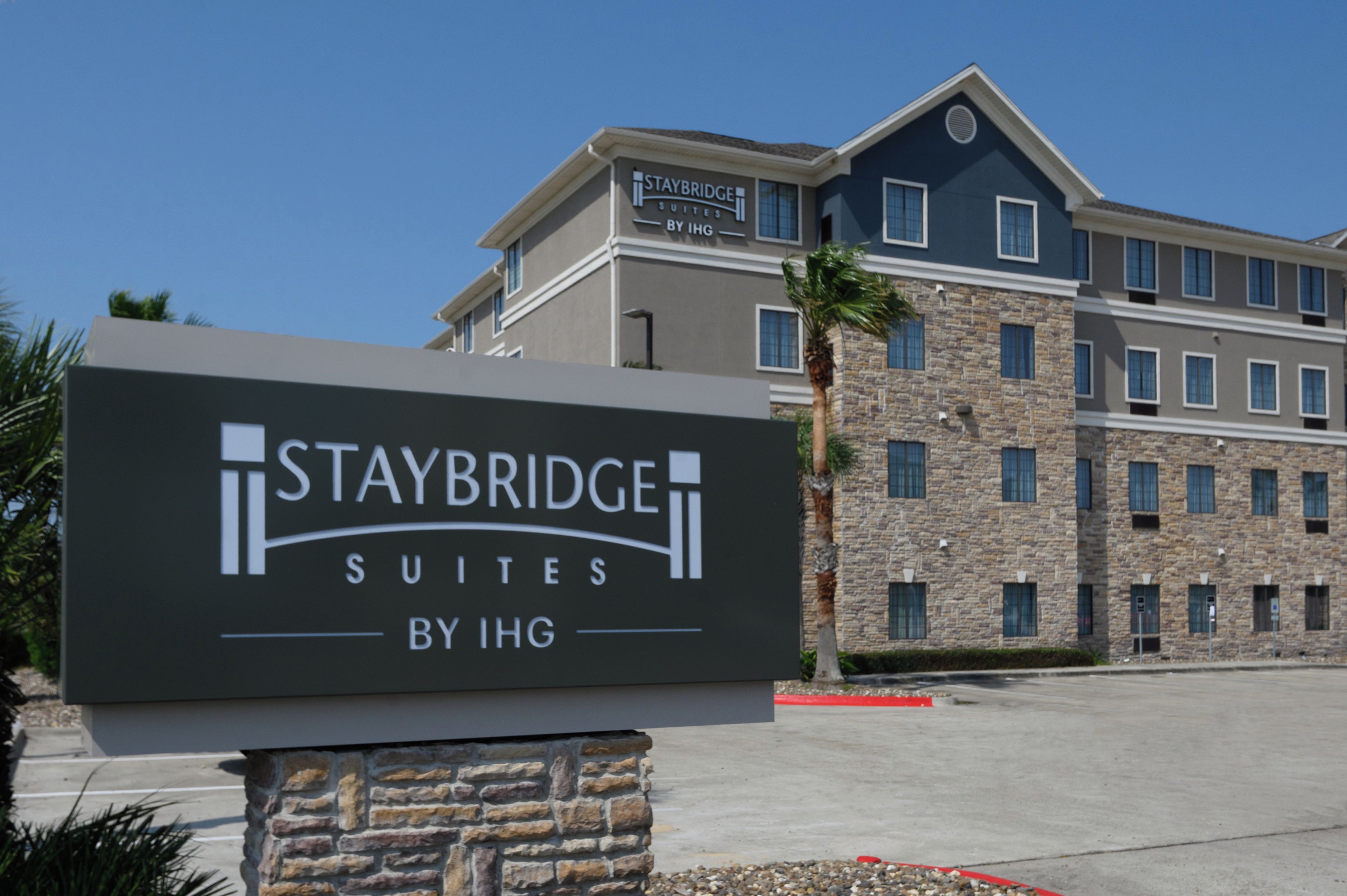 A sign for Staybridge Suites by IHG with a stone building in the background.