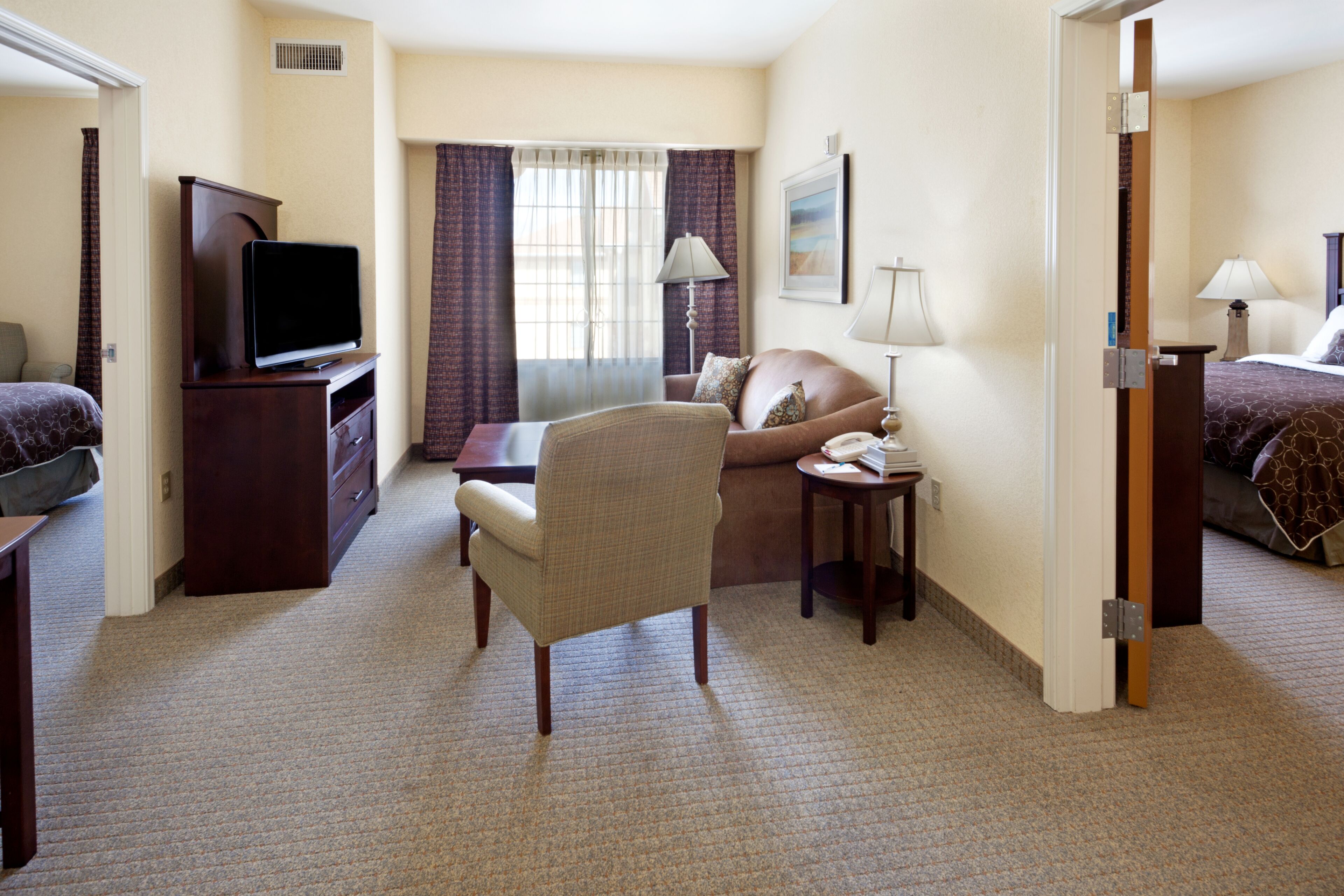 Habitación de hotel con cama, sillón, escritorio, televisor, lámpara y un cuadro en la pared.