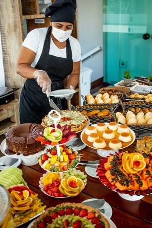 A buffet with various food items including a chocolate cake, fruit, and pastries. - Hotel Pousada Brava Club (Búzios)