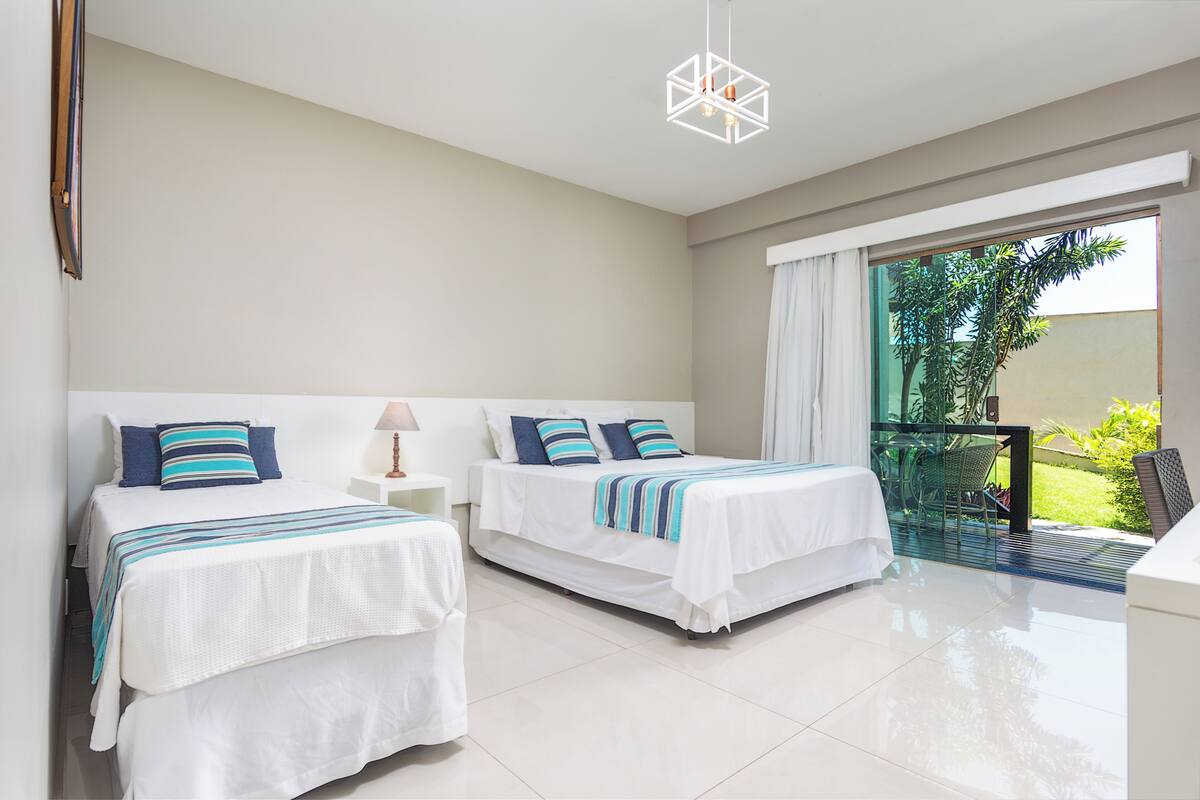 A hotel room with two beds, a balcony, and a modern chandelier.