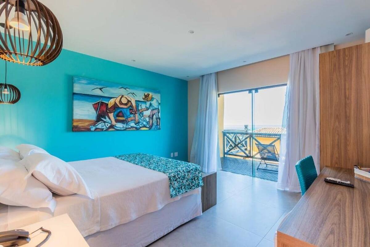 A bedroom with a bed, a desk, a painting, and a balcony with a view.