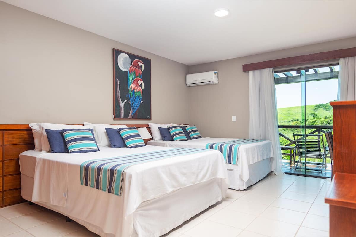 A hotel room with two beds, a painting of a parrot, an air conditioning unit, and a balcony with a view.