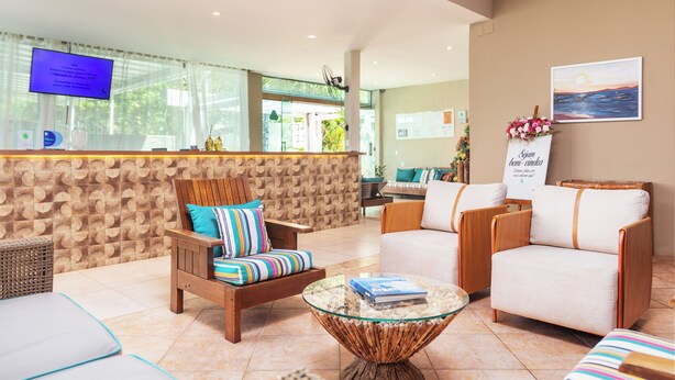 Un área de recepción con una televisión, muebles de mimbre, una mesa de centro de vidrio y una pared con un cuadro enmarcado.