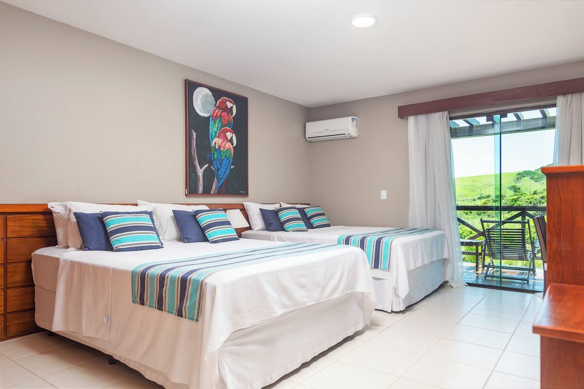 A hotel room with two beds, a painting of parrots, an air conditioner, and a balcony with a view.