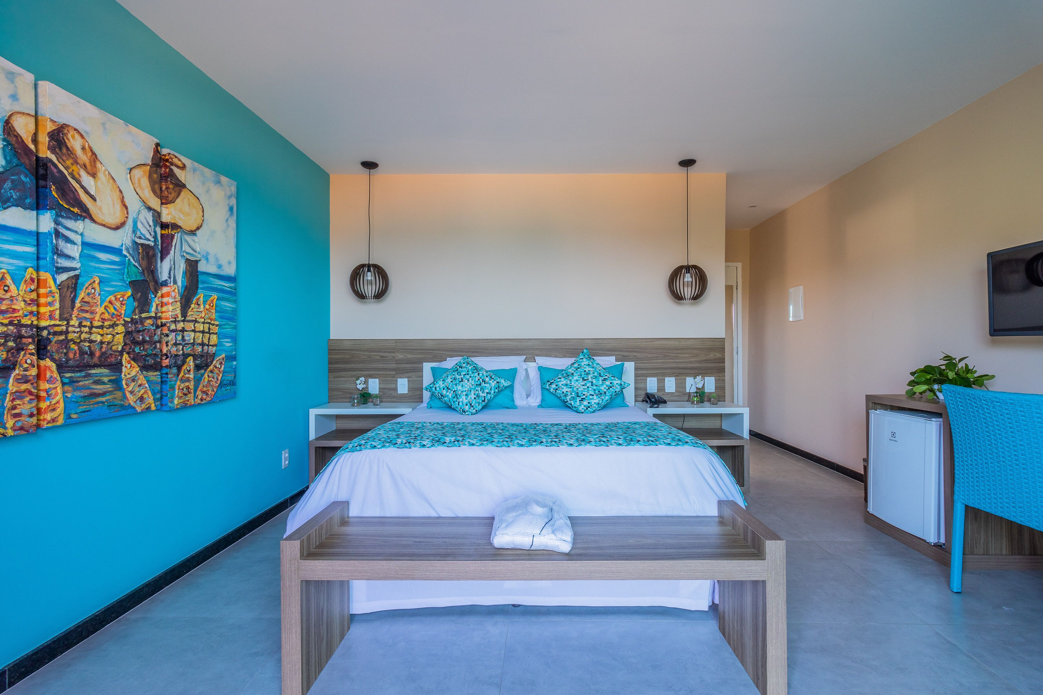 Habitación de hotel moderna con una cama grande, un escritorio, un refrigerador pequeño y un televisor montado en la pared.