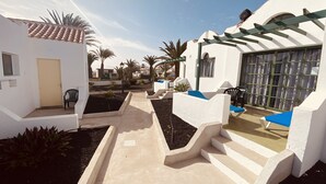 Une cour bordée de bâtiments blancs, agrémentée d’une pergola et dotée d’un espace salon extérieur.