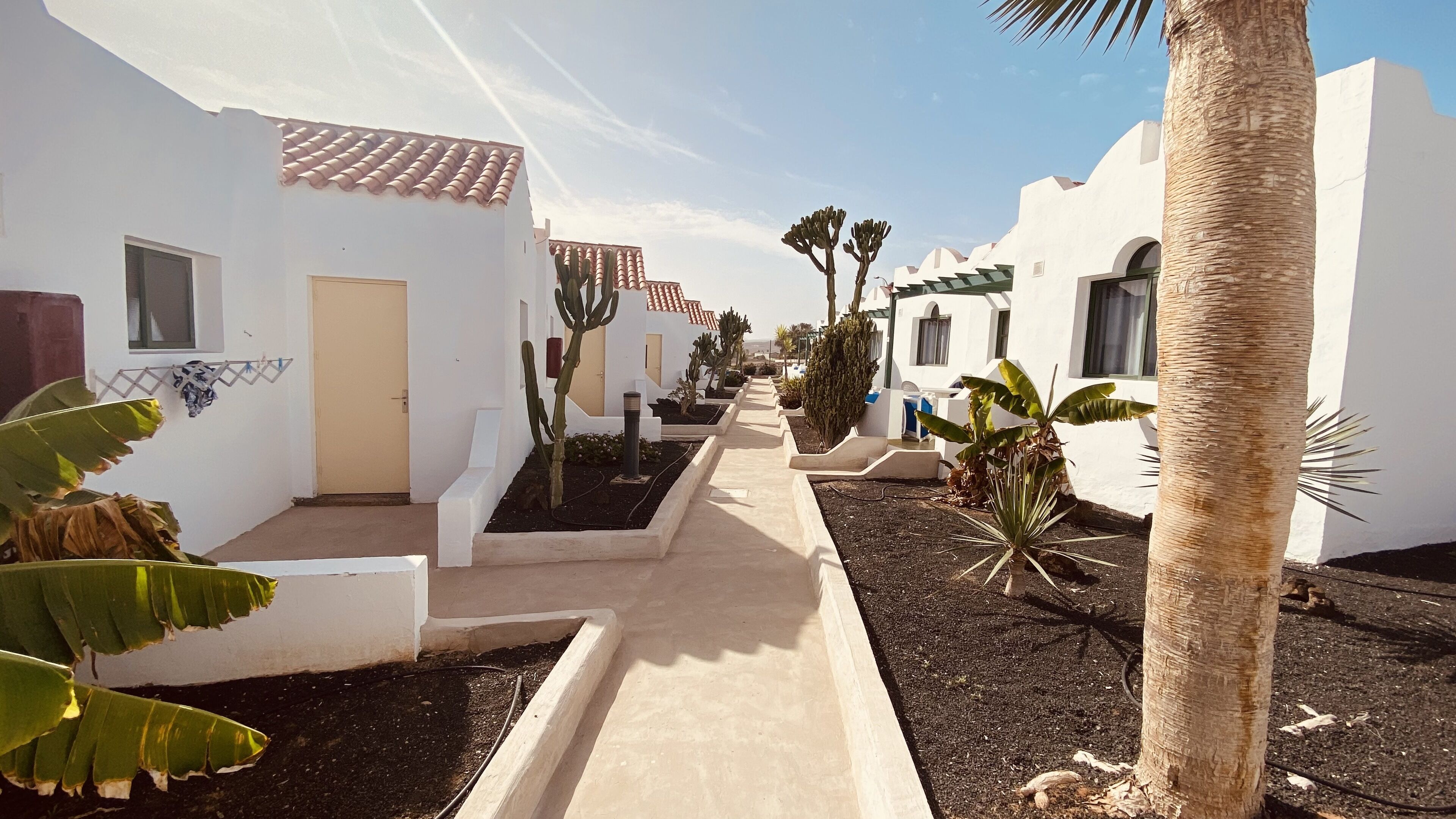 A pathway flanked by white buildings with terracotta roofs, leading to a gate.