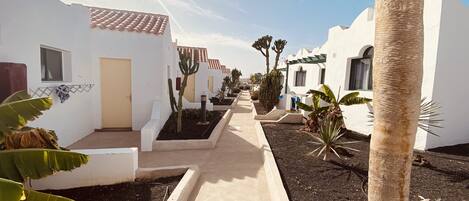 A pathway flanked by white buildings with terracotta roofs, leading to a gate.
