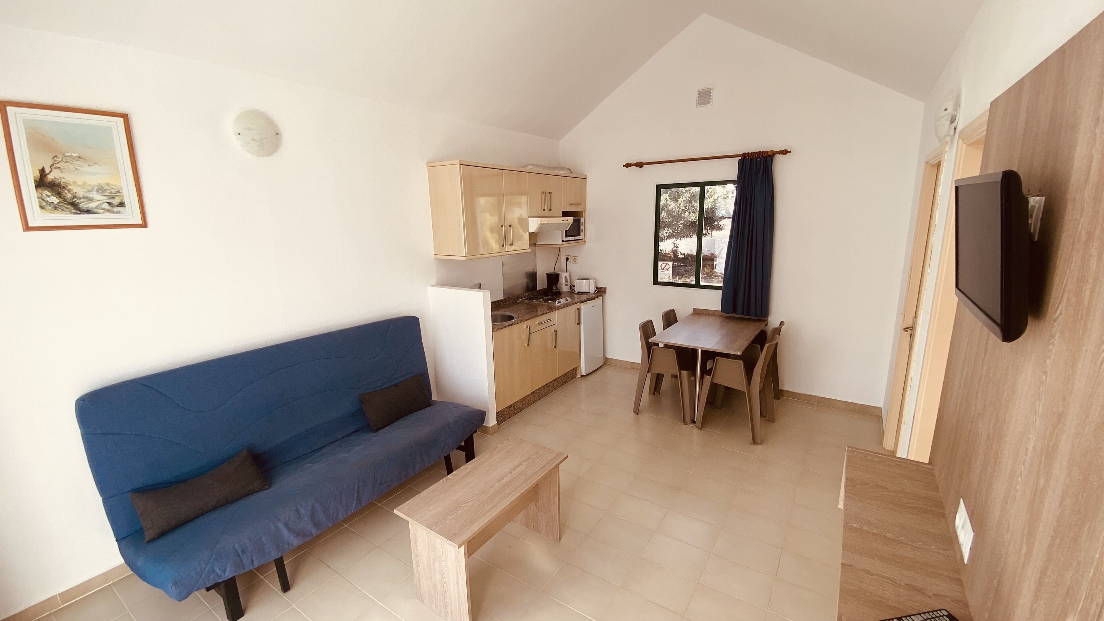 Un espacio habitable compacto con sofá, una mesa de comedor, una cocina y un televisor.