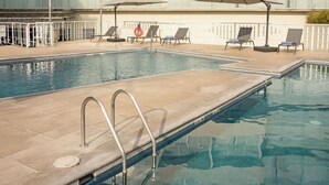 A swimming pool with a tiled deck, lounge chairs, and umbrellas. - Holiday Inn Express Guadalajara Expo by IHG (Guadalajara)