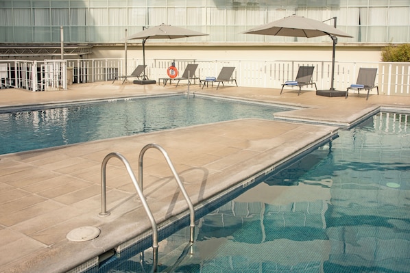 A swimming pool with a tiled deck, lounge chairs, and umbrellas. - Holiday Inn Express Guadalajara Expo by IHG (Guadalajara)