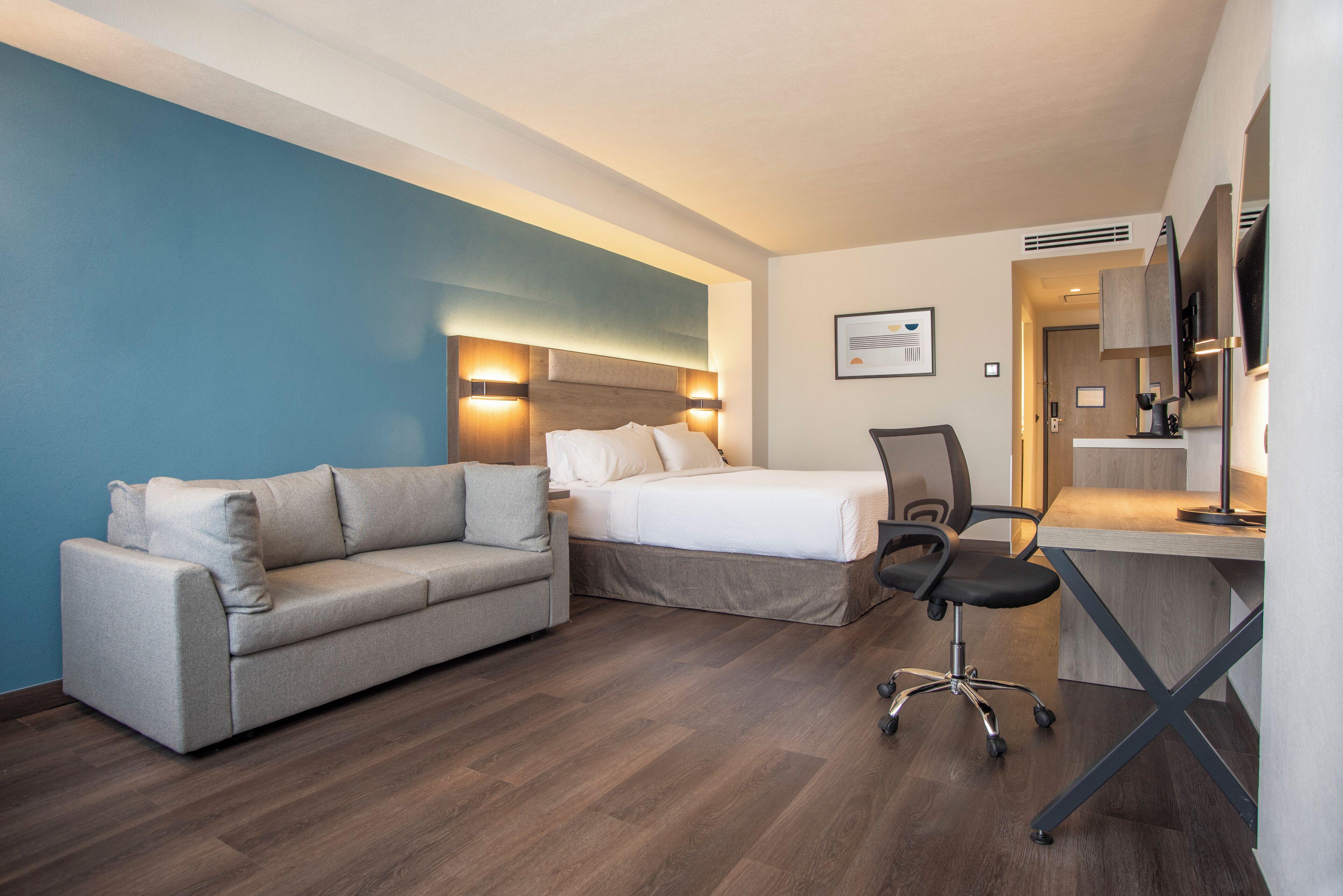 A hotel room with a bed, a sofa, a desk, and a chair.