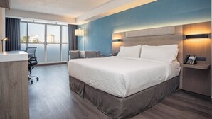 A hotel room with a large bed, a desk, a chair, and a view of the city through large windows. - Holiday Inn Express Guadalajara Expo by IHG (Guadalajara)