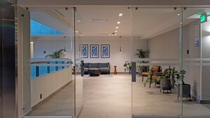 A modern lobby with a reception desk, seating area, and potted plants.