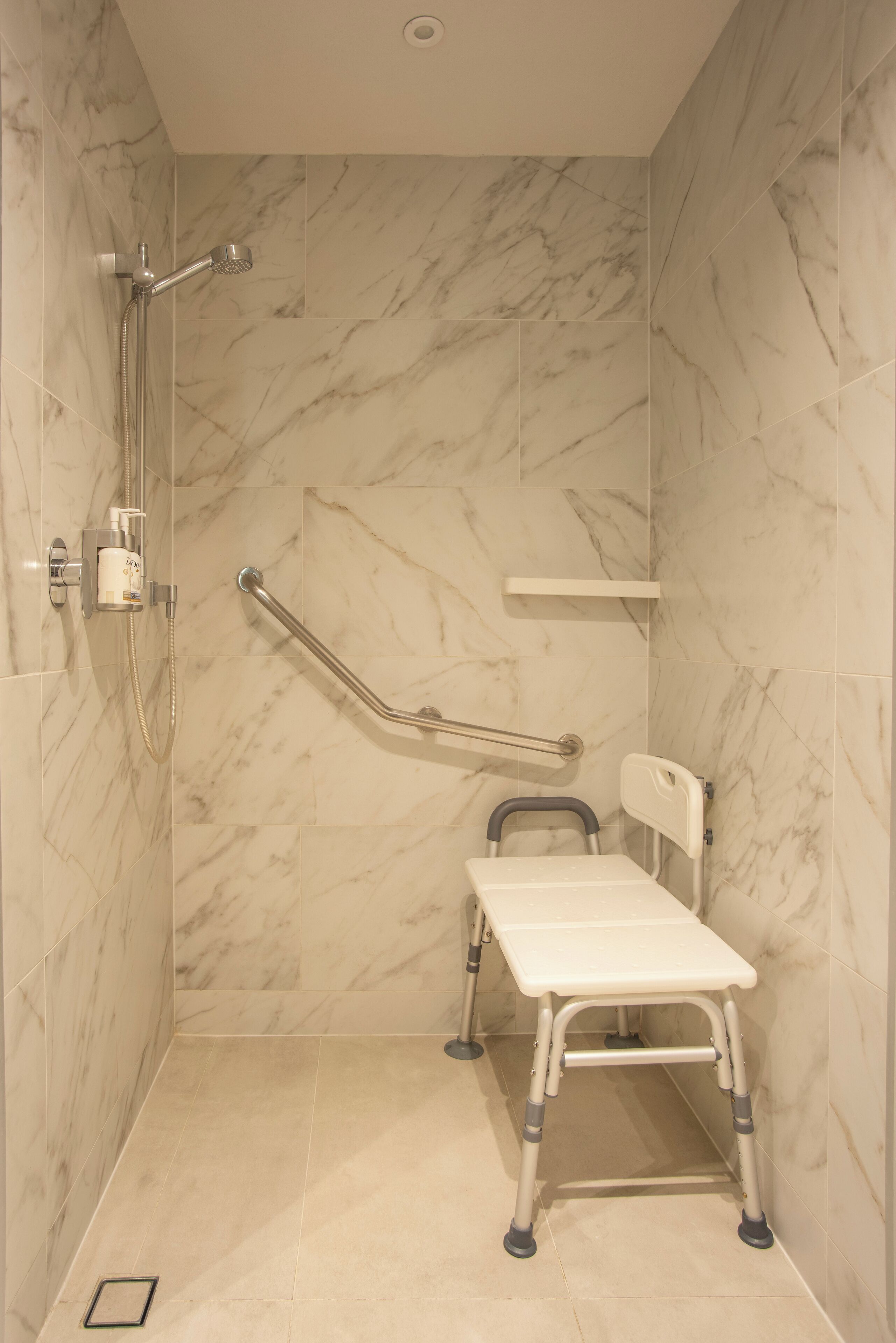 A bathroom with a shower, grab bars, a wheelchair-accessible bench, and marble walls.