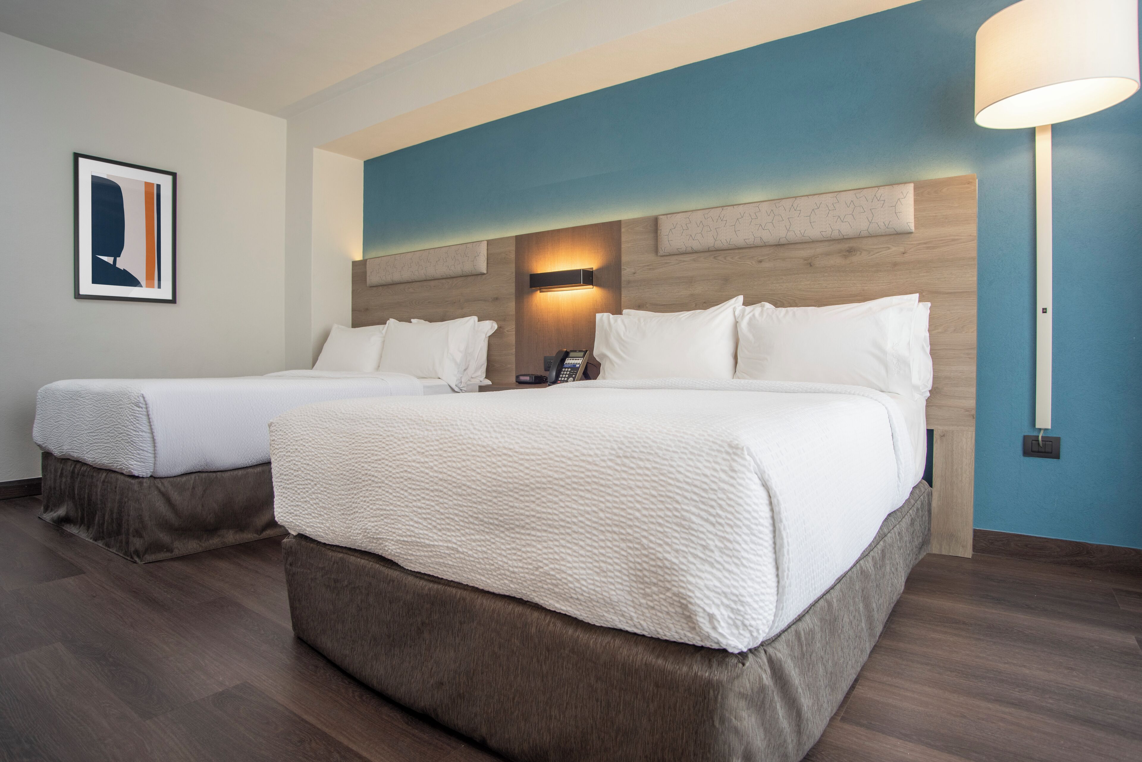 A hotel room with two beds, a wall-mounted phone, and a nightstand.