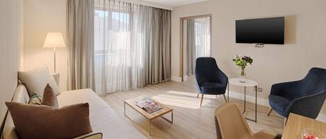 A hotel room with a sofa, two armchairs, a coffee table, a TV, and a small table with a vase.