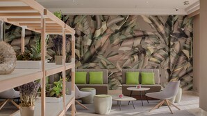 A modern lounge area with a sofa set, two armchairs, a coffee table, and a shelving unit with plants. - NH Nice (Nice)