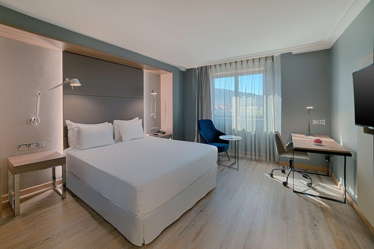 A hotel room with a large bed, bedside tables, a desk with a chair, and a TV.