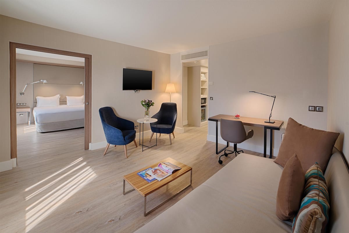 A hotel room with a bed, two armchairs, a desk, a coffee table, and a TV.