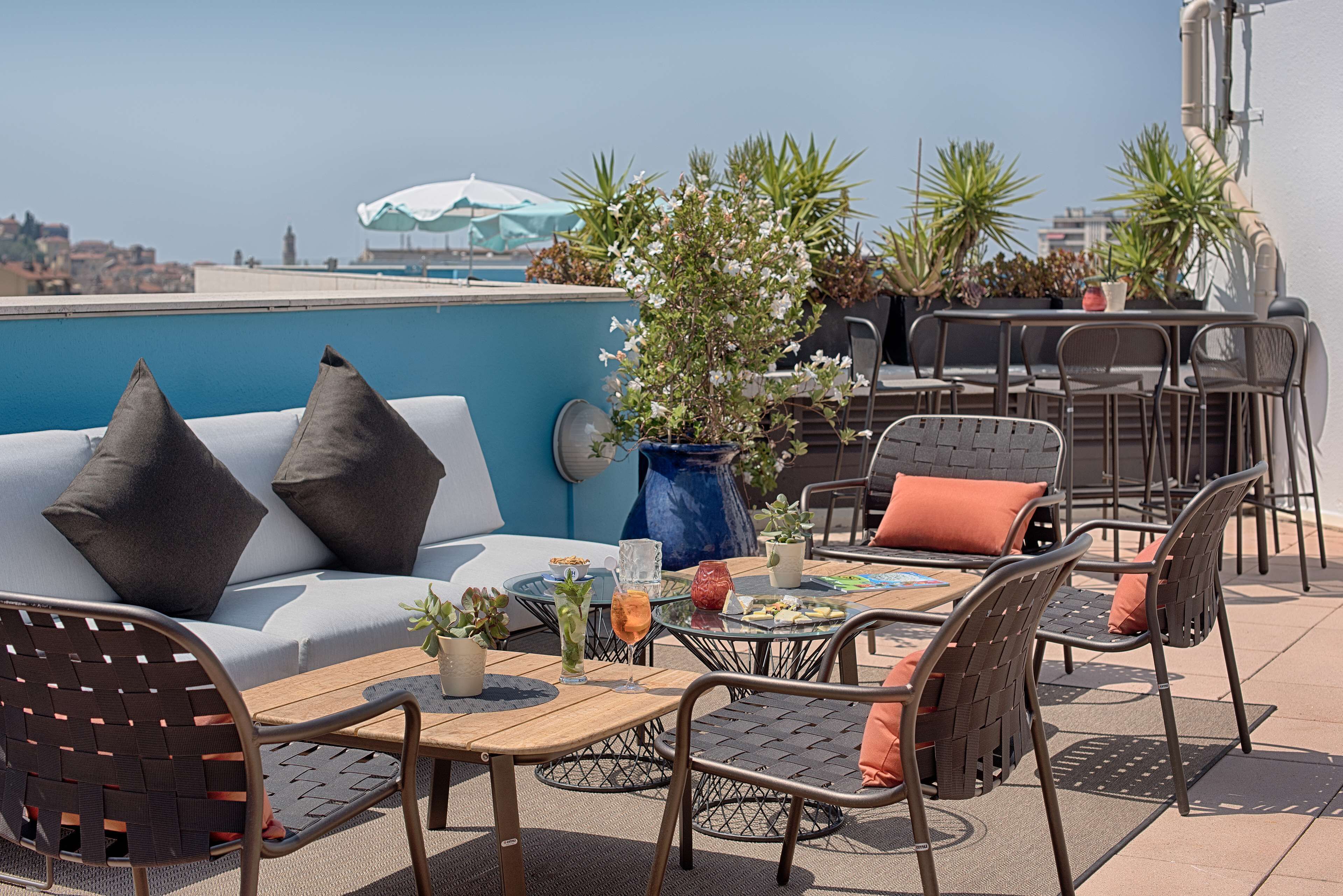 A rooftop terrace with a sofa, chairs, a table, and potted plants.