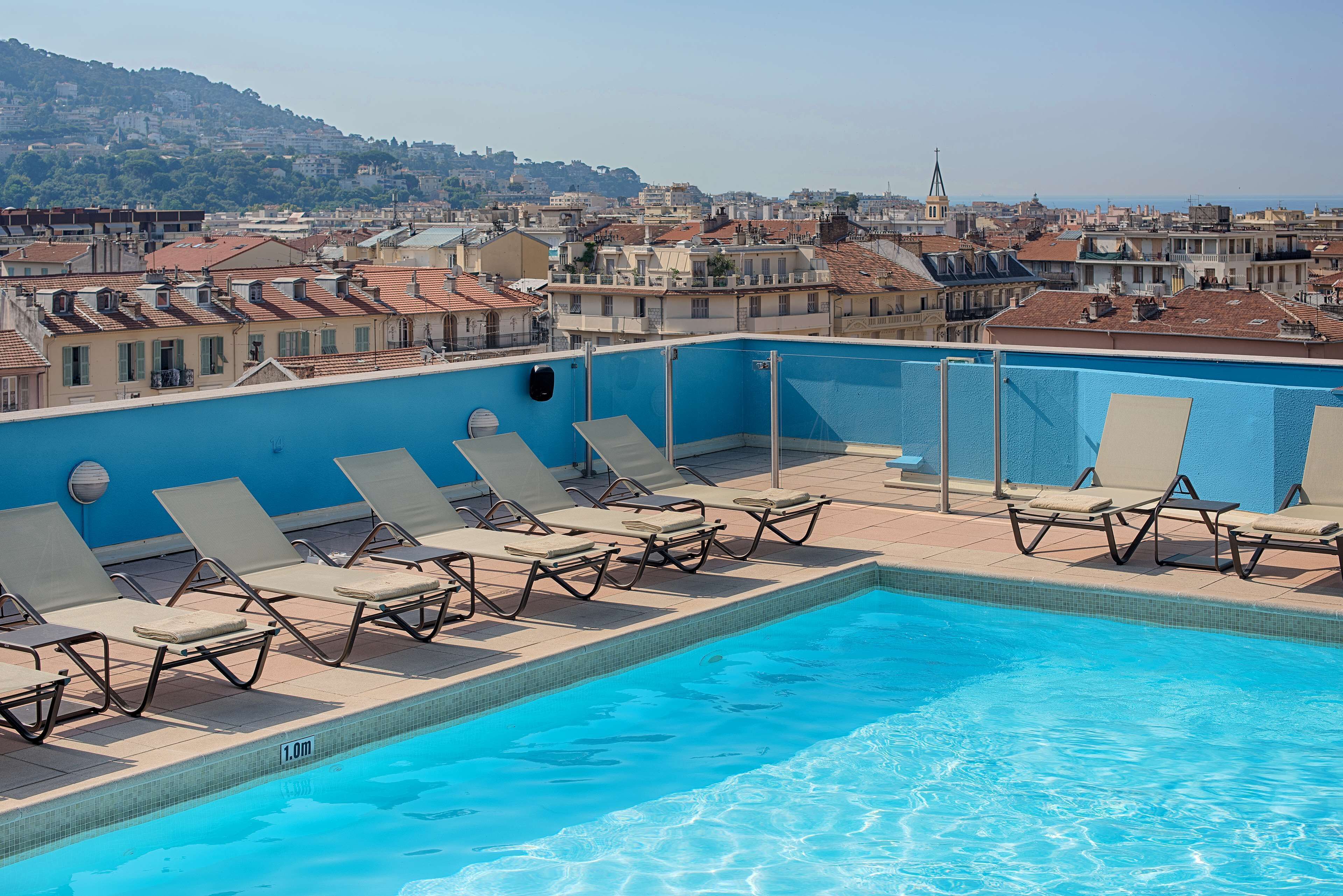 Une piscine sur le toit, dotée de chaises longues et offrant une vue sur le paysage urbain.