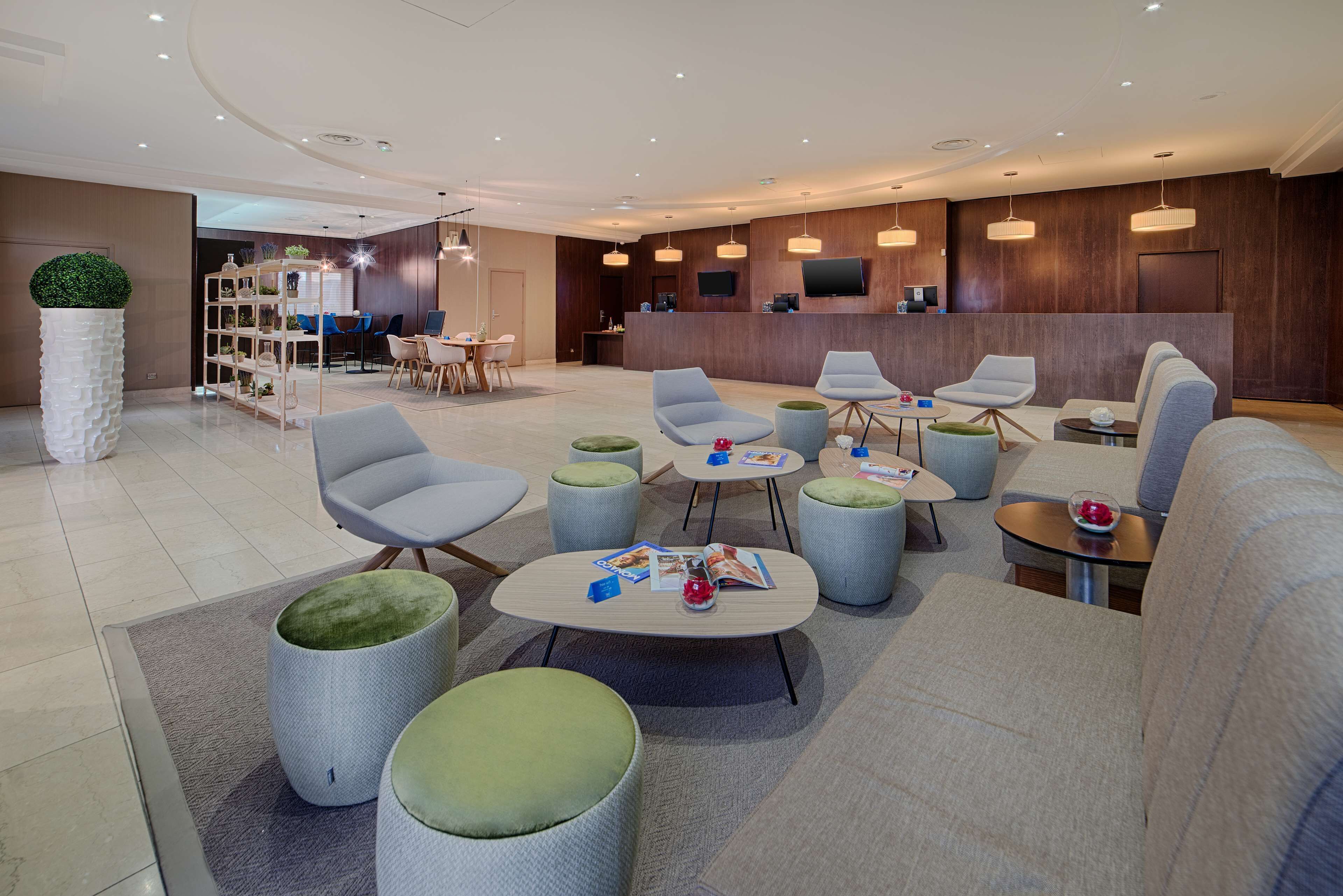 A modern hotel lobby with seating areas, a reception desk, and a dining area.