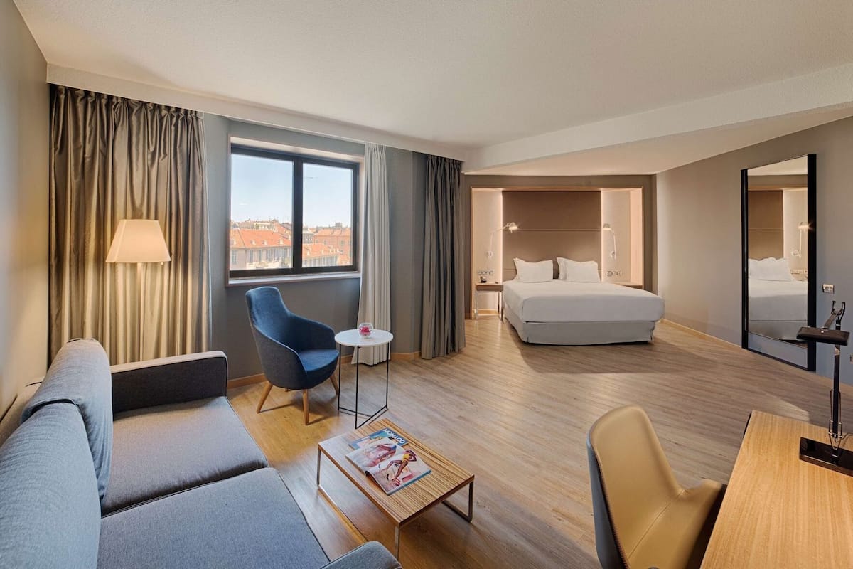 A hotel room with a sofa, armchair, small table, and a bed.