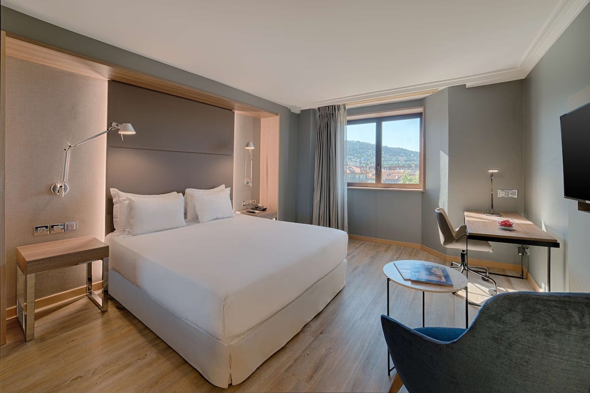 A hotel room with a large bed, bedside tables, a desk, and a chair.