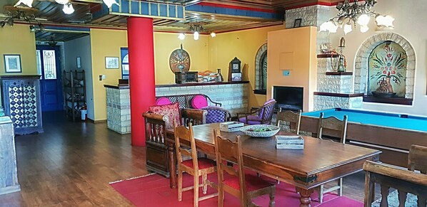 Un espace repas avec une table et des chaises en bois, un pilier rouge et une cheminée.