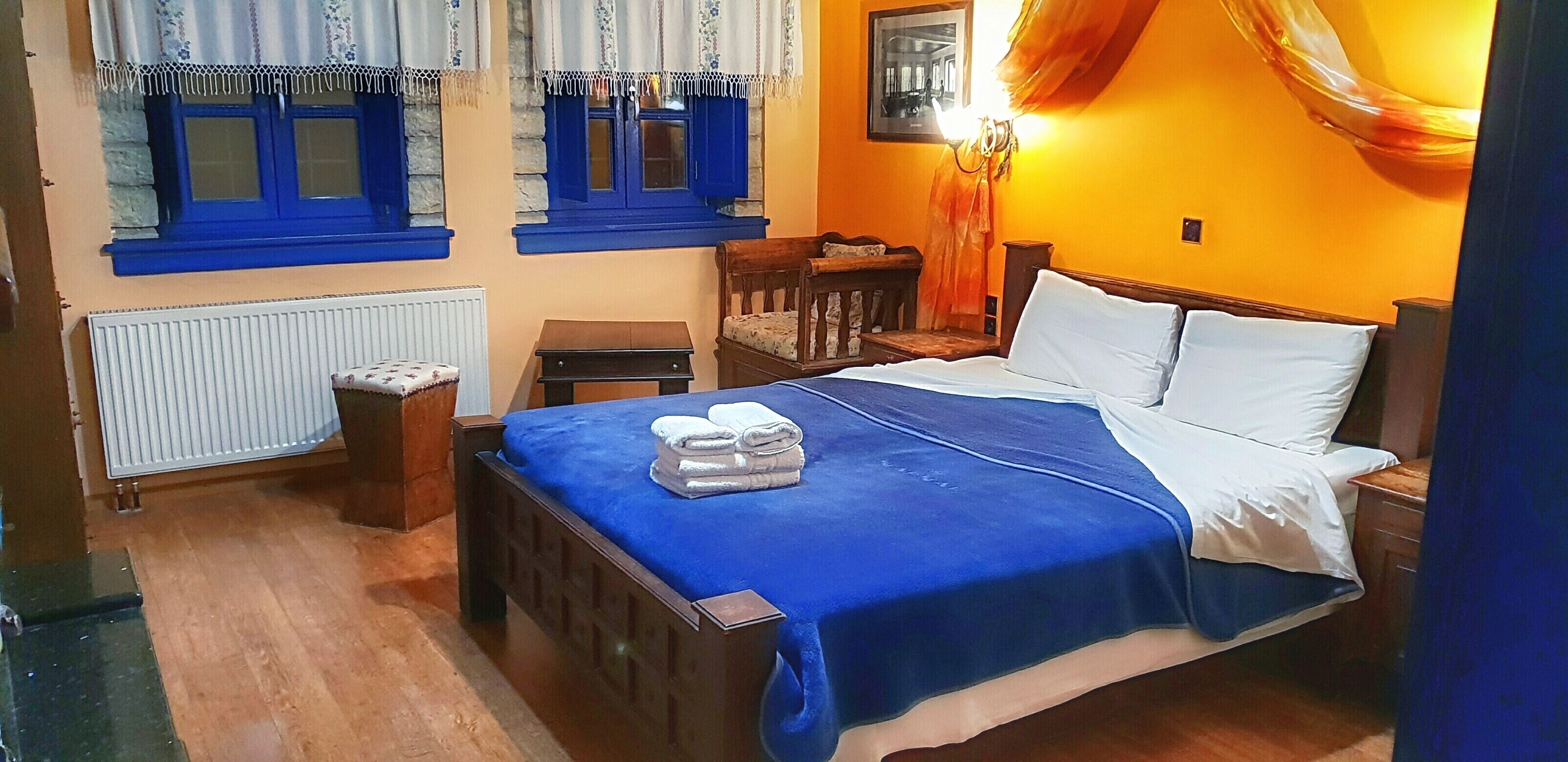 A bedroom with a bed, a nightstand, a chair, a table, and a window with blue shutters.