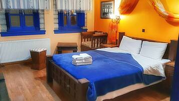A bedroom with a bed, a nightstand, a chair, a table, and a window with blue shutters.