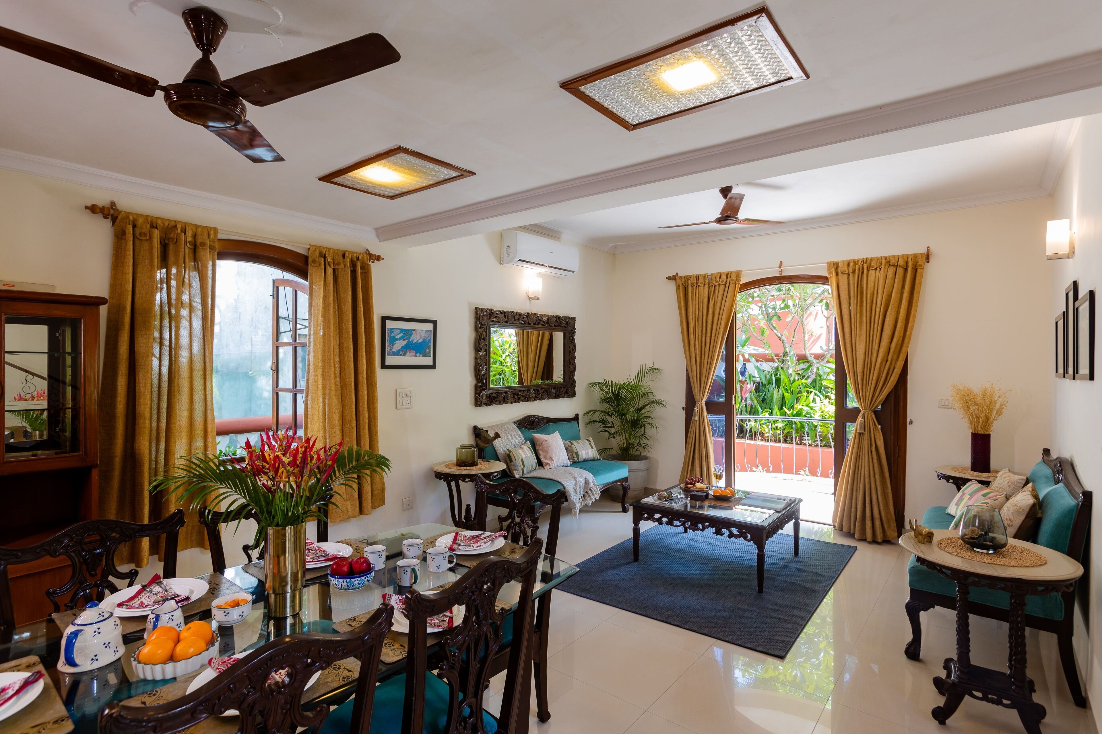 A spacious living room with a dining area, featuring a ceiling fan, large windows with curtains, a sofa, and a coffee table.