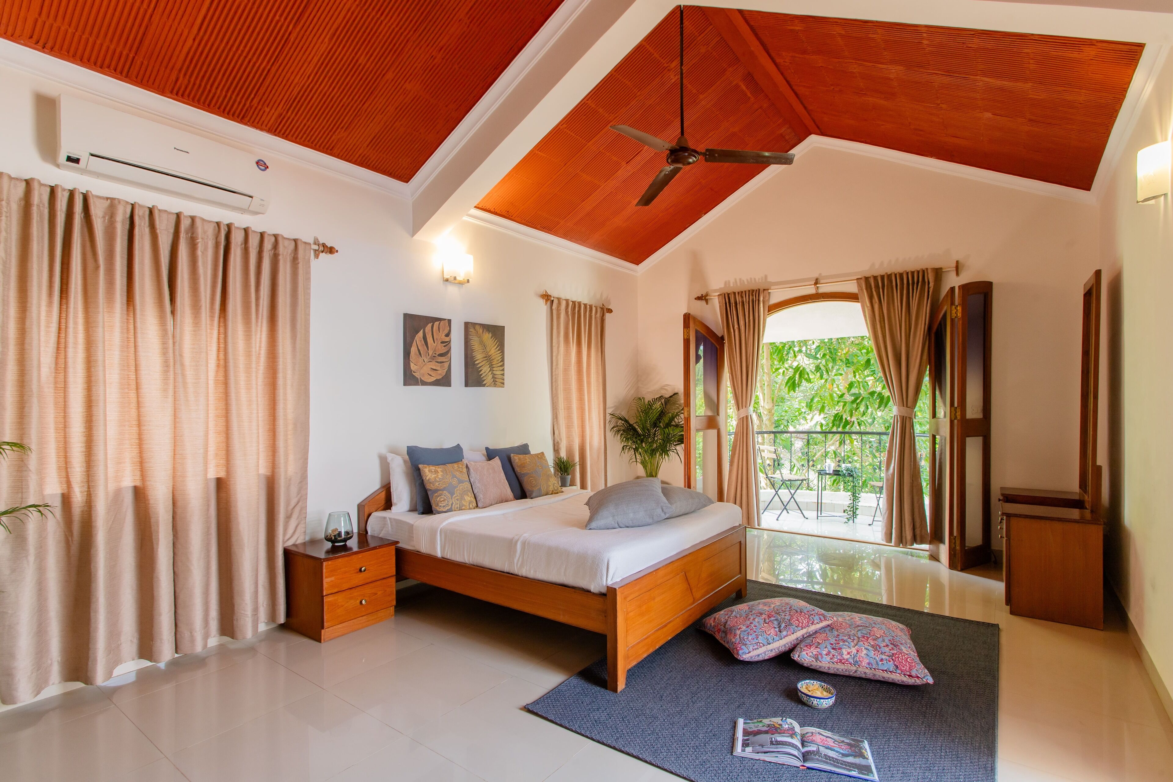 A bedroom with a wooden ceiling, a bed, a nightstand, a window with curtains, and a view of greenery outside.