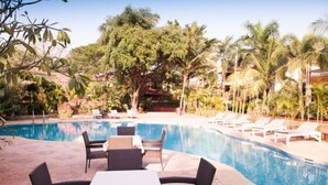 A swimming pool with lounge chairs and tables, surrounded by palm trees and greenery. - Aguada Anchorage - The Villa Resort (Candolim)