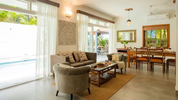 A spacious living room with a large sofa, coffee table, and dining area with chairs and a table. - Aguada Anchorage - The Villa Resort (Candolim)