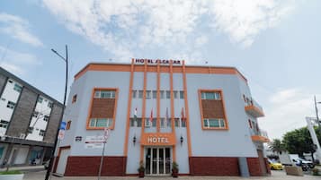 Un hotel con una entrada destacada, varias banderas y un letrero que indica zona de no estacionamiento.