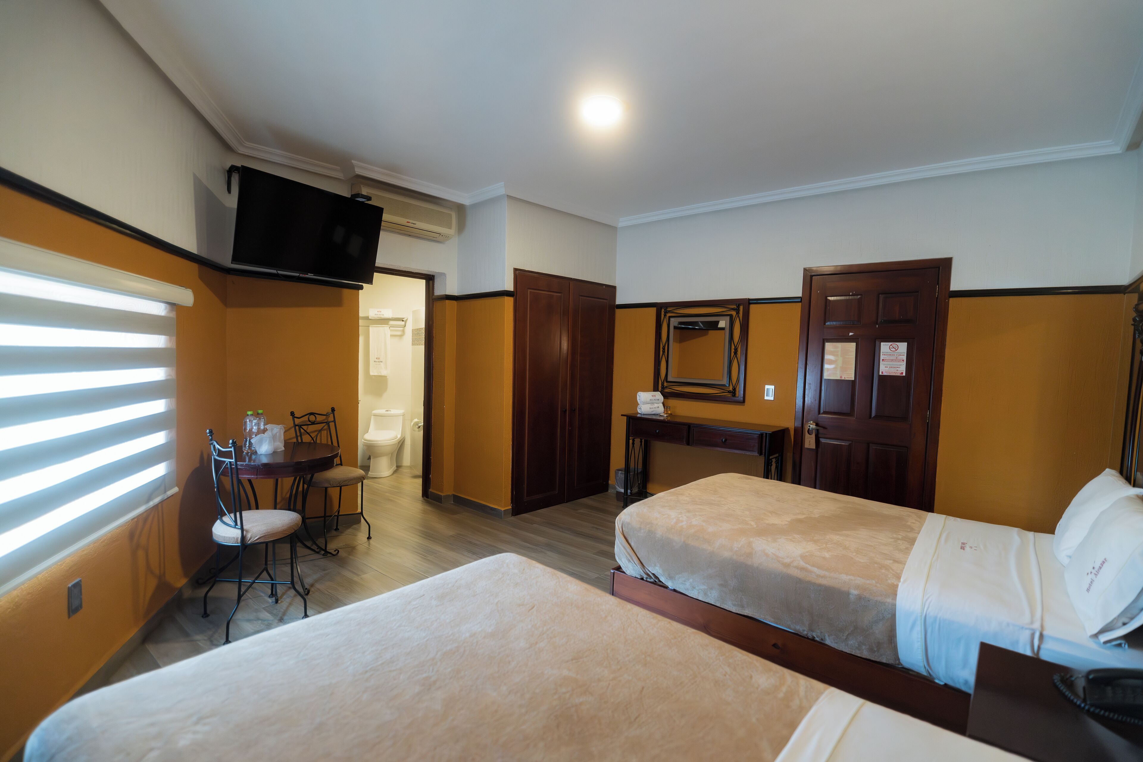 A hotel room with two beds, a desk, a chair, a TV, and a bathroom.