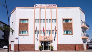 A hotel with a white facade, a sign reading "HOTEL ALCAZAR," and two potted plants at the entrance. - Hotel Alcazar (Guadalajara)