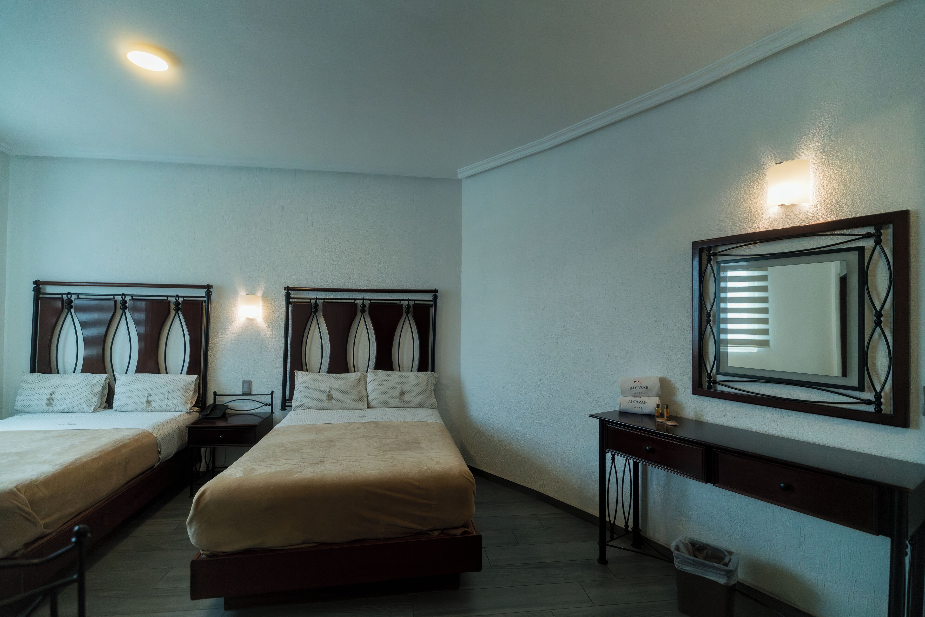 Een hotelkamer met twee bedden, een bureau, een prullenbak en een grote spiegel.
