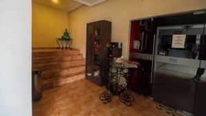 Vestíbulo de hotel con una escalera, una mesa de vidrio con patas metálicas decorativas y un letrero que dice 'Jale' en la puerta.