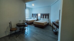 A hotel room with two beds, a small table with chairs, a desk, and a trash bin. - Hotel Alcazar (Guadalajara)