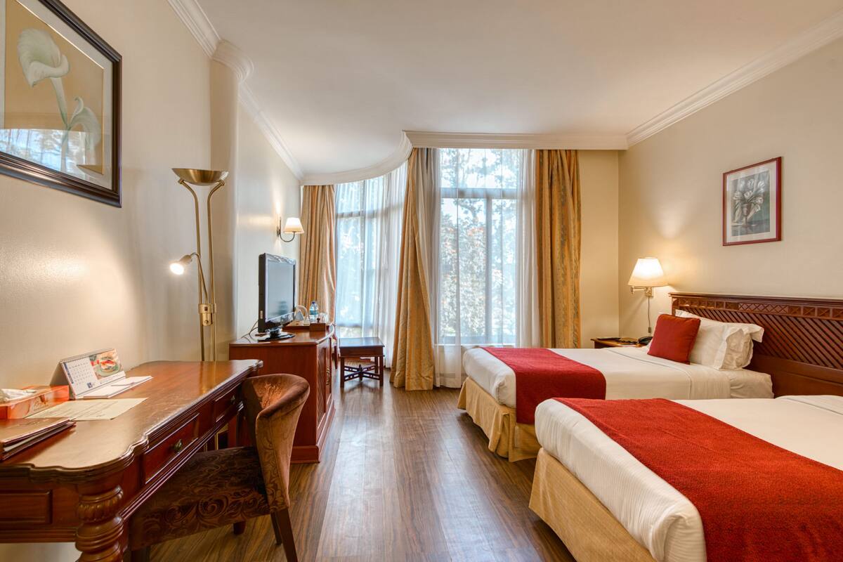 A hotel room with two beds, a desk, a chair, a TV, and a window with curtains.