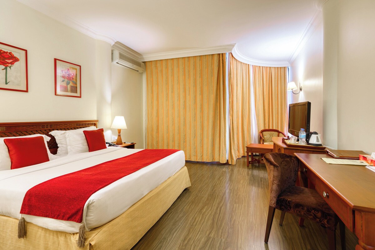 A hotel room with a large bed, a desk, a chair, a television, and a window with curtains.